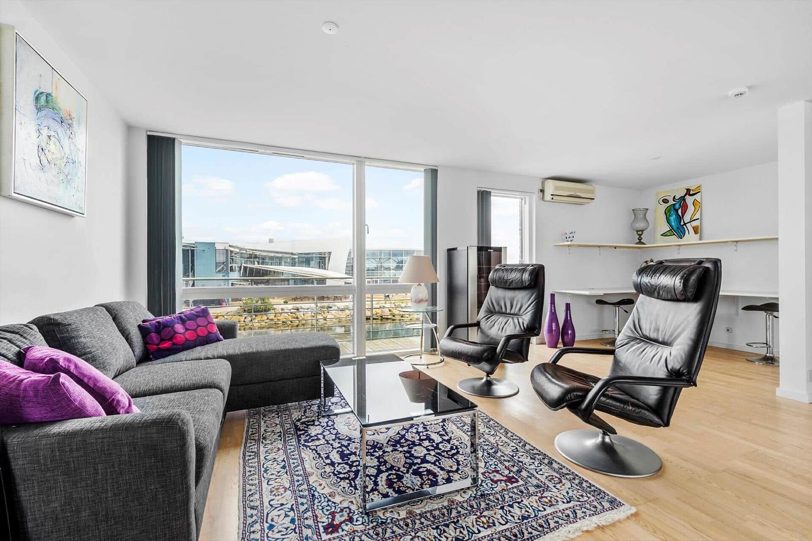 Wohnzimmer mit Sofa, zwei Sessel und Blick auf den Hafen.