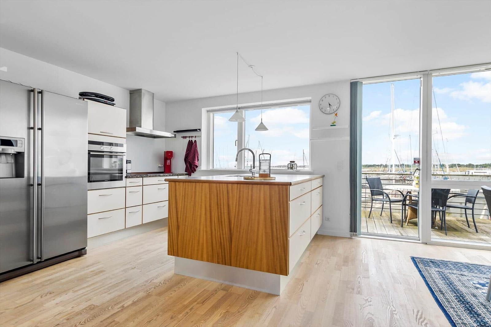 Küche mit Insel, Blick auf Hafen und Terrasse mit Stühlen.