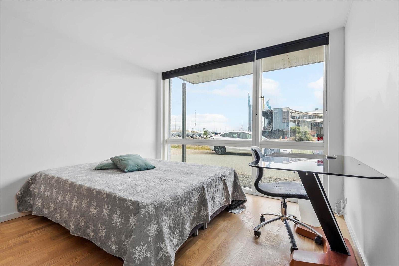 Schlafzimmer mit Bett, Schreibtisch und großem Fensterblick.