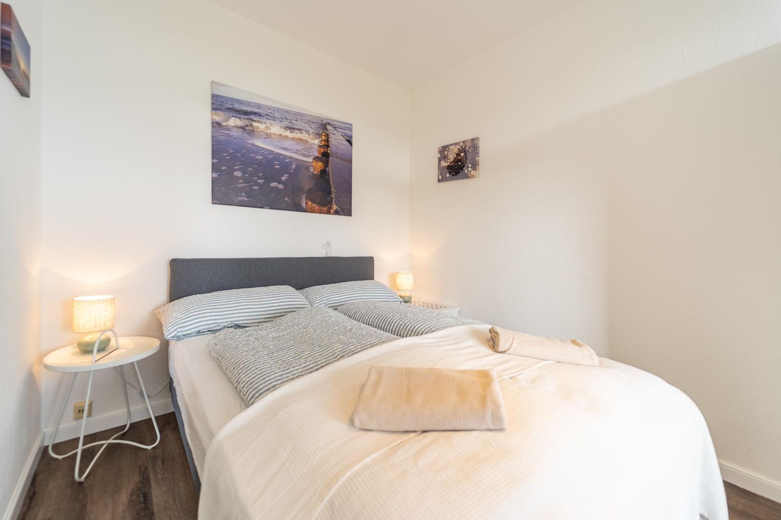 Schlafzimmer mit Bett, Nachttischen und Wandbildern.