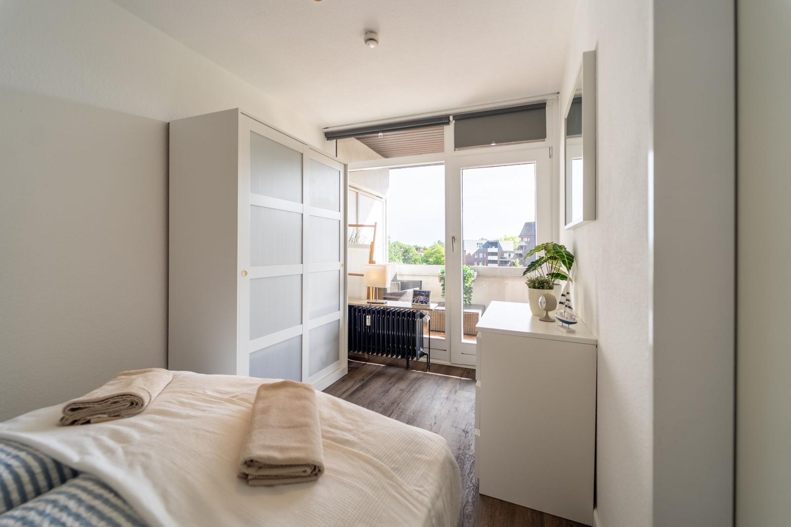 Schlafzimmer mit Bett, Kleiderschrank und Balkonzugang.