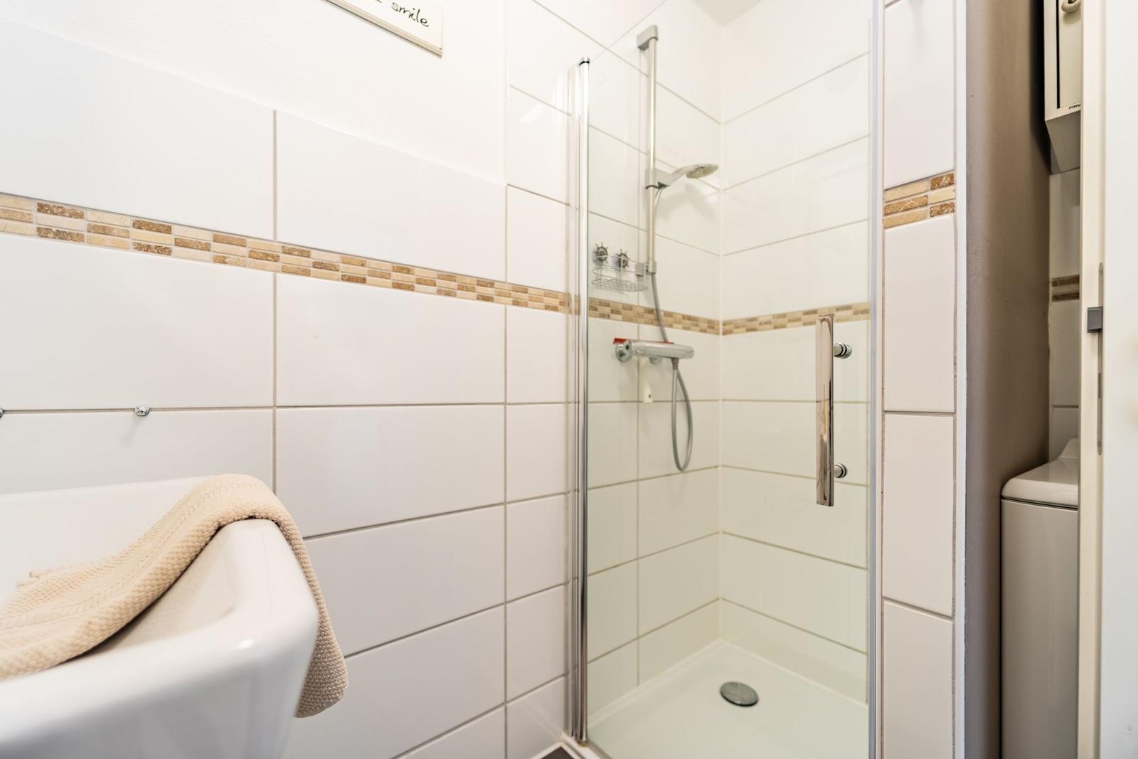 Badezimmer mit Dusche und Badewanne. Weiße Fliesen mit braunen Akzenten.