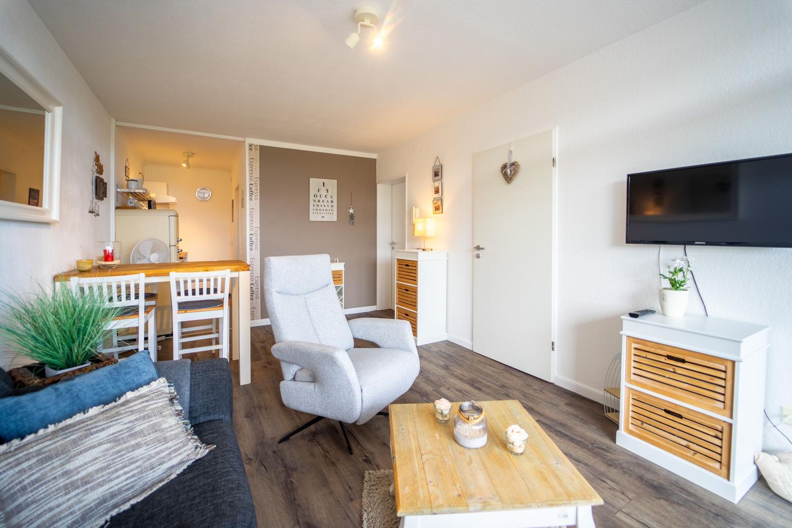 Wohnbereich mit Sofa, Sessel, Esstisch und Fernseher an der Wand.