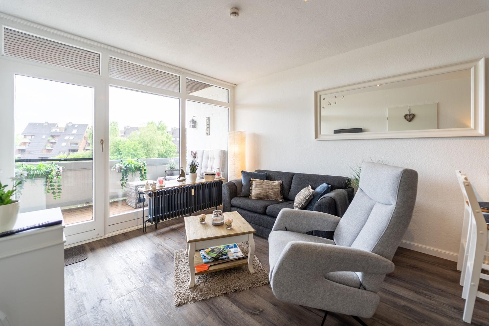 Wohnzimmer mit Sofa, Sessel und Terrasse. Holzfußboden und große Fenster.