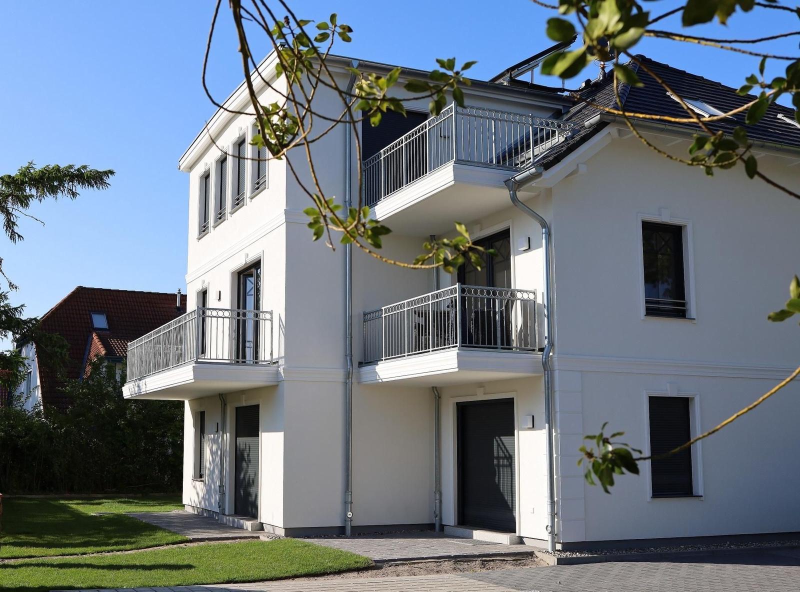 Modernes Haus mit Balkonen und grünem Grundstück.