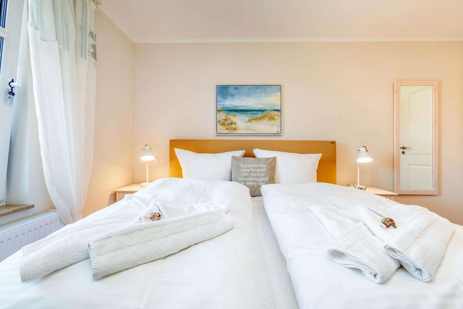 Zwei Betten mit weißen Bettwäschen und Handtüchern. Wandbild und Spiegel sind sichtbar.
