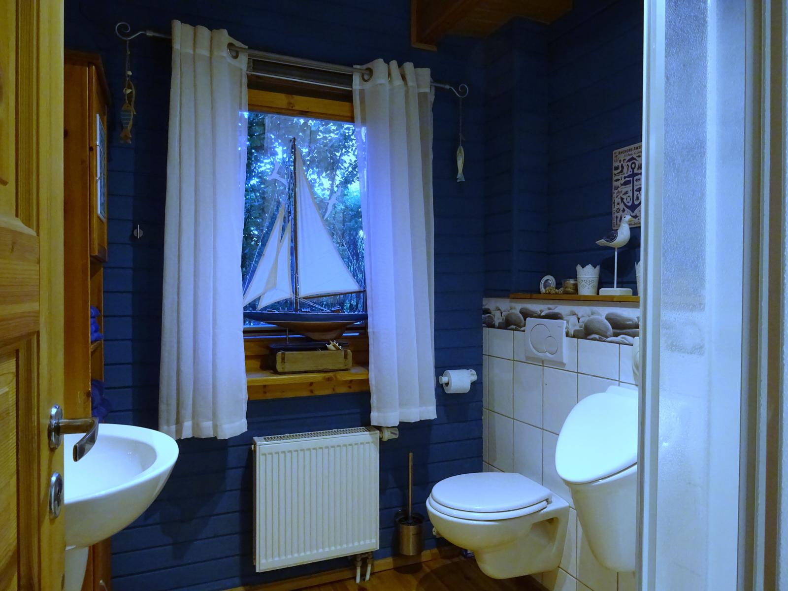 Badezimmer mit blauen Wänden, Fenster mit Segelbootmodell und Toilette.