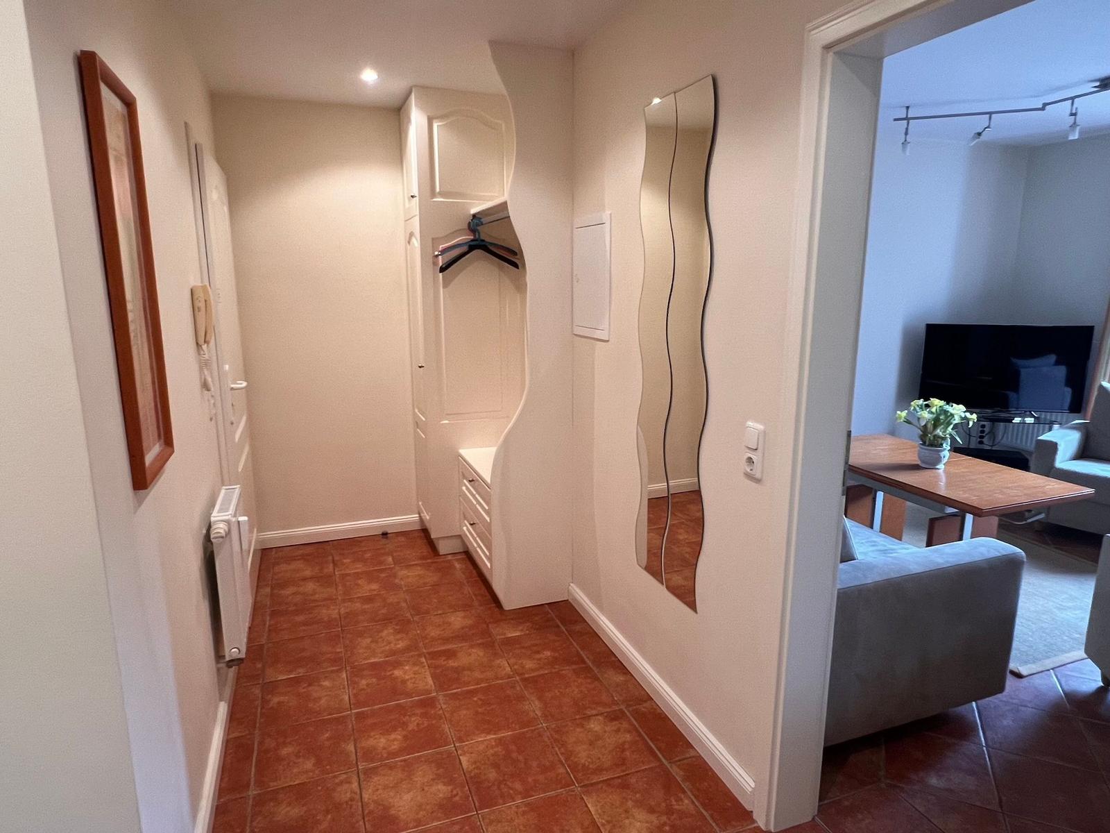 Flur mit Kleiderschrank und Spiegel, Blick in Wohnzimmer mit Sofa und TV.