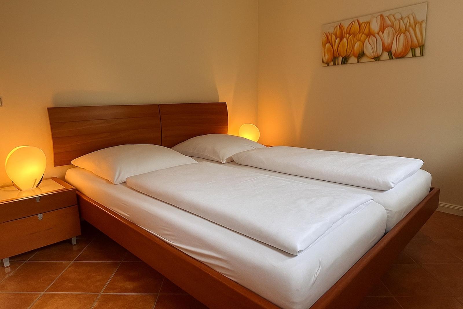 Doppelbett mit weißen Bettwäsche, Nachttisch und Wandbild mit Tulpen.