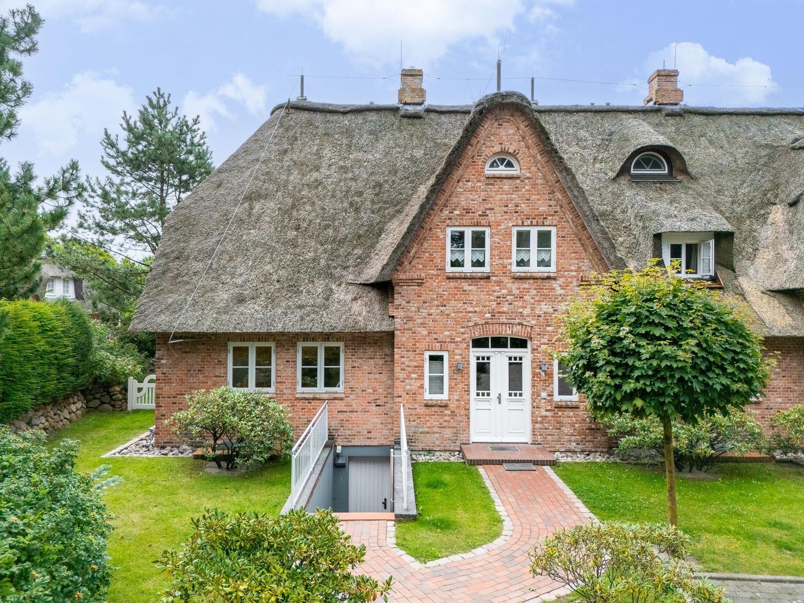 Rotes Backsteinhaus mit Strohdach und weißer Eingangstür. Grün umgeben mit gepflastertem Weg.