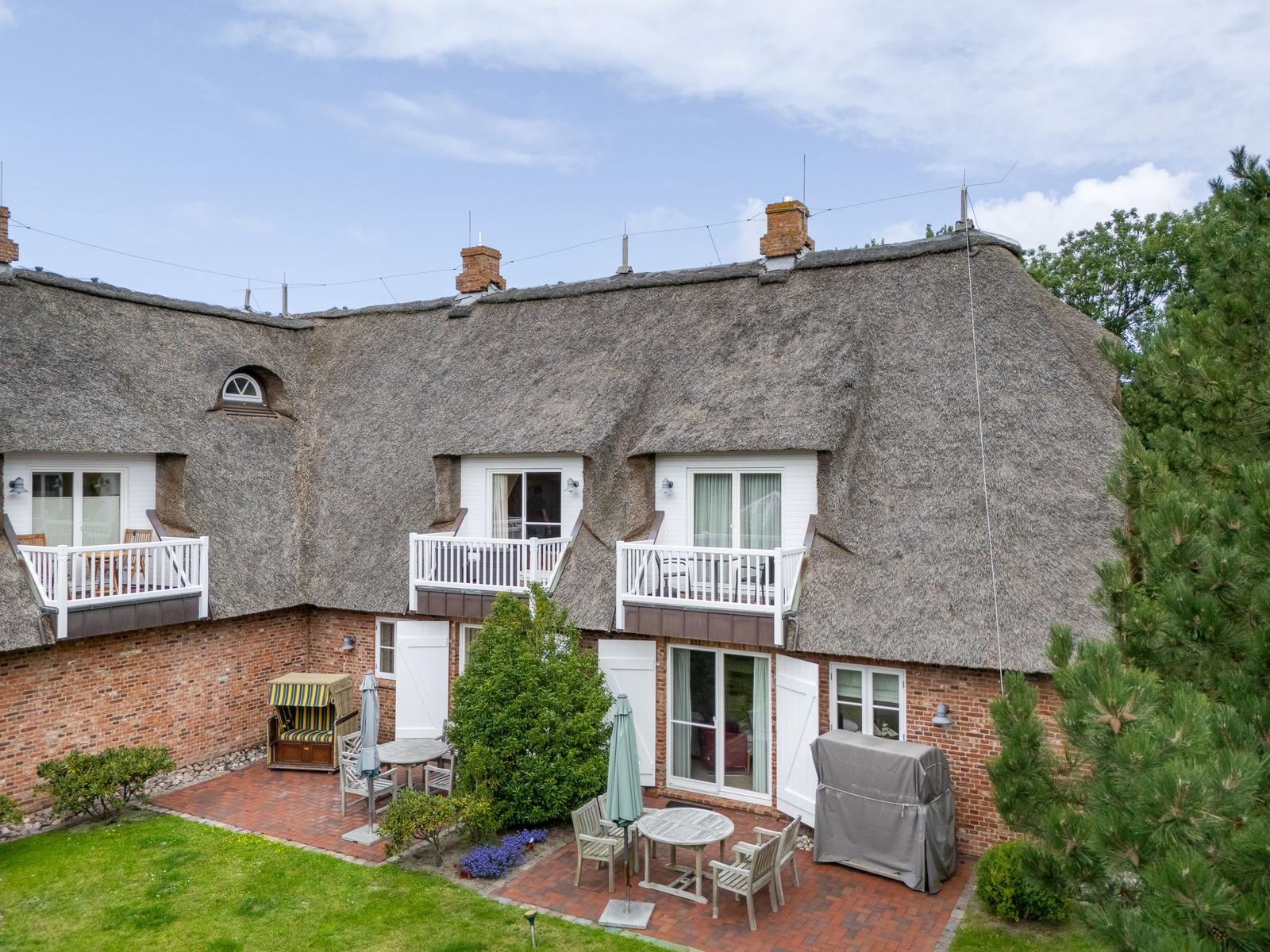 Haus mit strohgedecktem Dach und Balkonen. Gartenbereich mit Tischen und Stühlen.