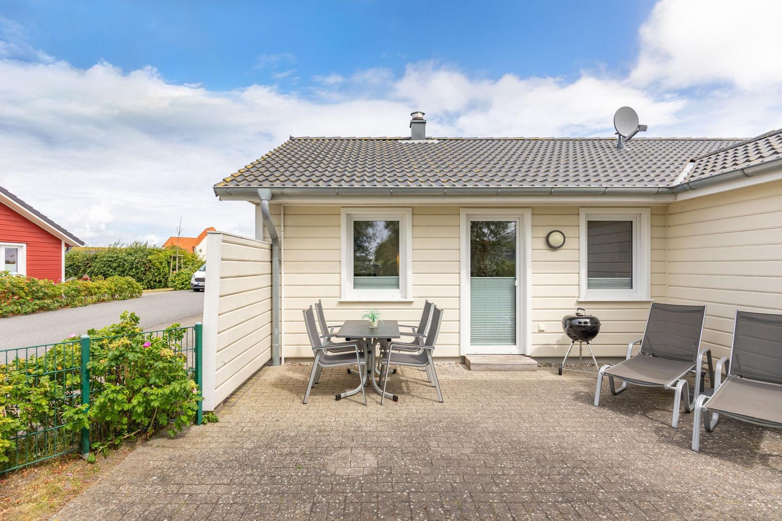 Haus mit Terrasse, Grill und Sitzgelegenheiten im Freien.