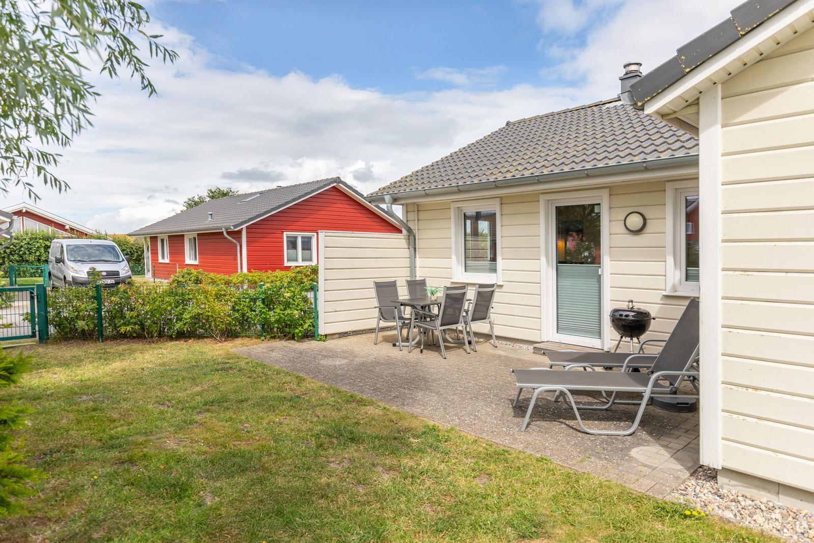Terrasse mit Tisch, Stühlen und Liegen neben einem hellen Haus.