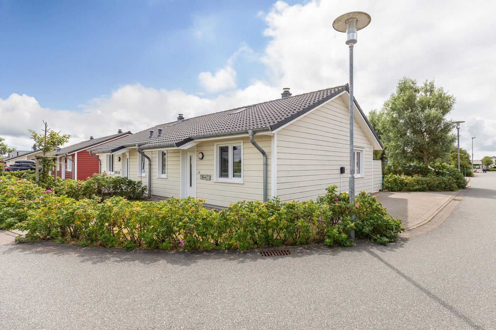 Ein hellbeiges Haus mit Dach und Fenstern. Umgeben von Grünflächen und einem Gehweg.