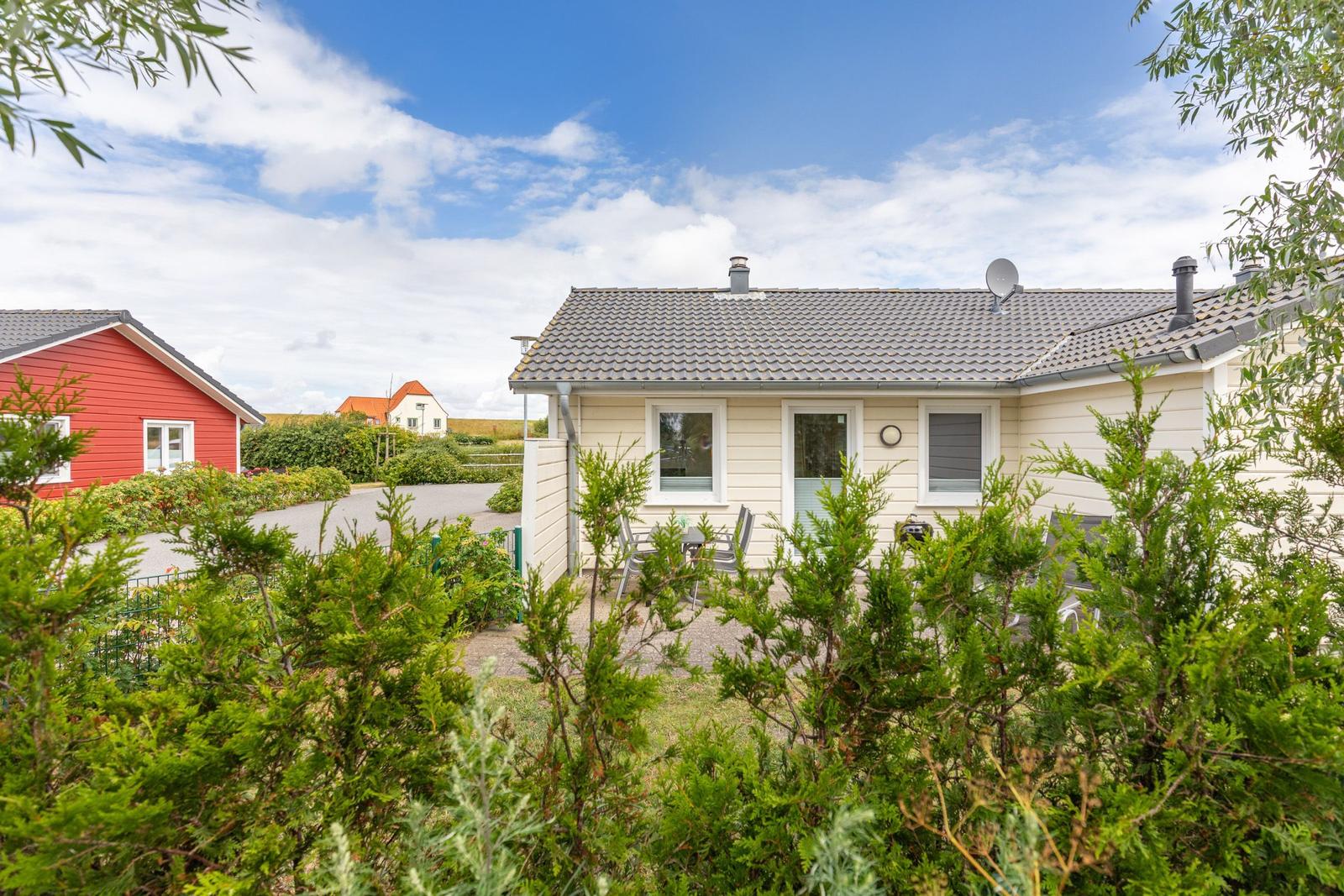 Ein weißes Ferienhaus mit Garten und Terrasse unter blauem Himmel.