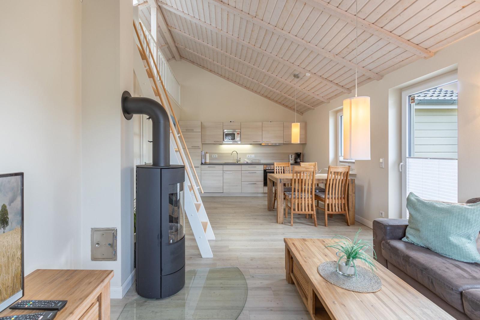 Wohnzimmer mit Esstisch, Küche und Kaminofen unter Holzdecke.