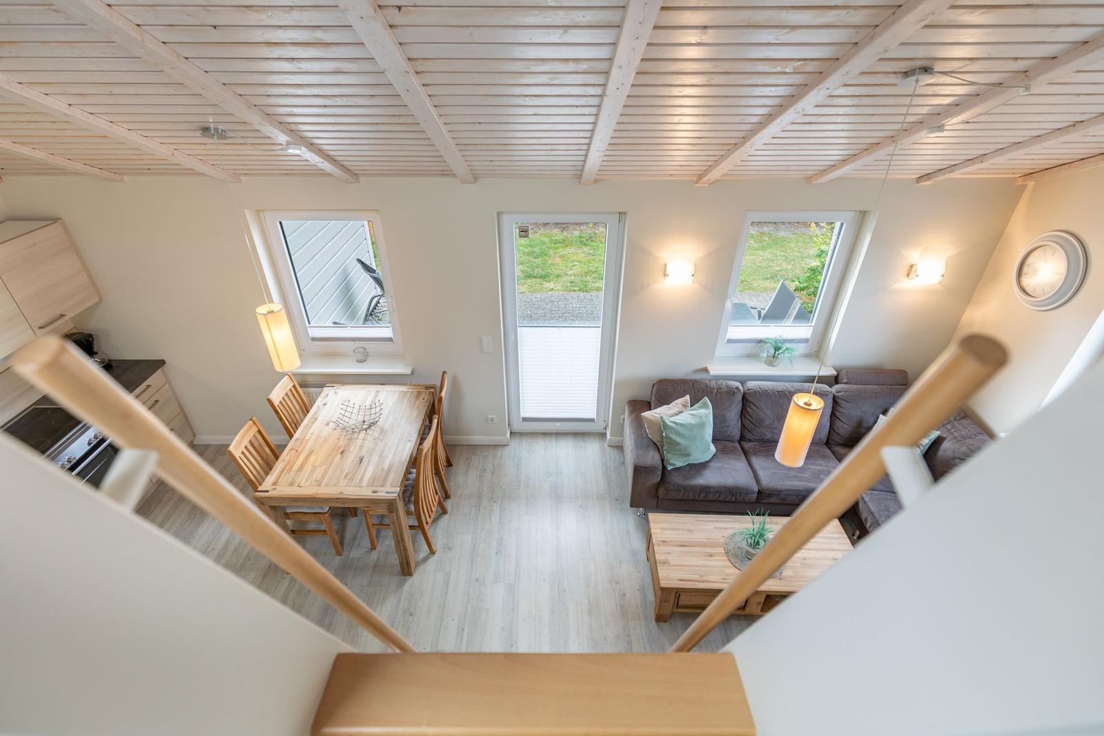 Wohn- und Essbereich mit Holzdecke, Sofa, Tisch und Fenstern.