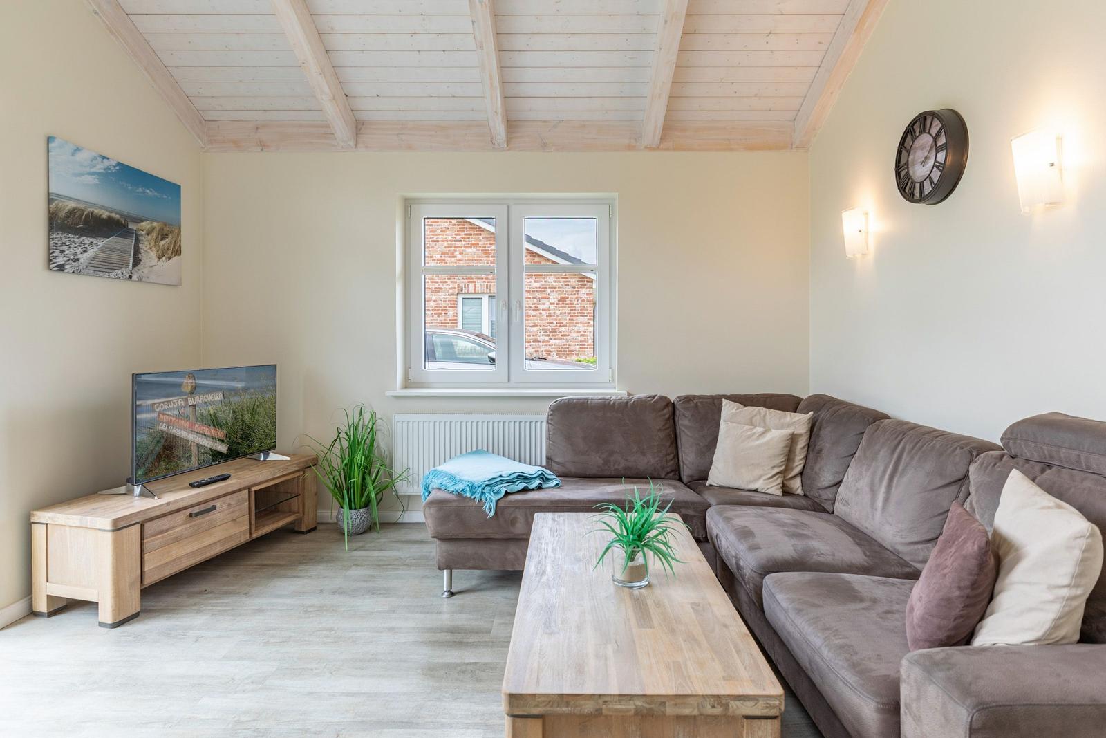 Wohnzimmer mit Sofa, Couchtisch und Fernseher. Holzdecke und Fenster mit Blick.