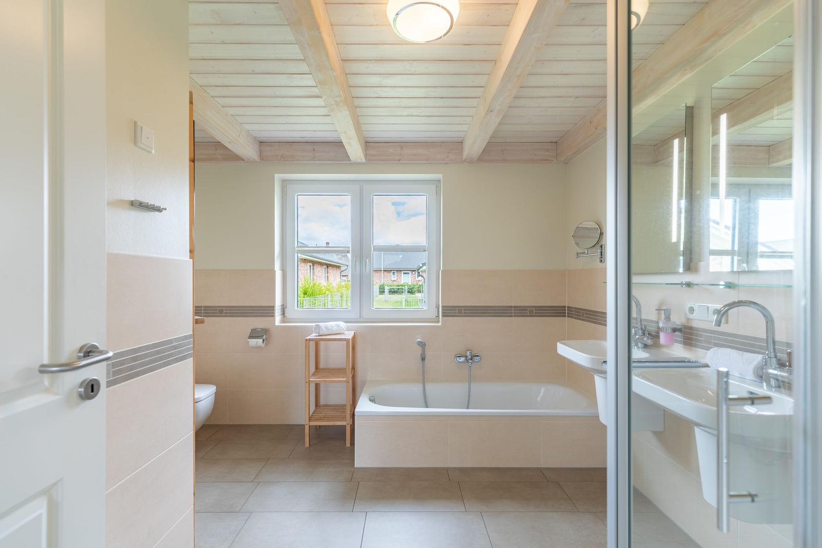 Badezimmer mit Badewanne, Dusche und Fenster mit Blick nach außen.