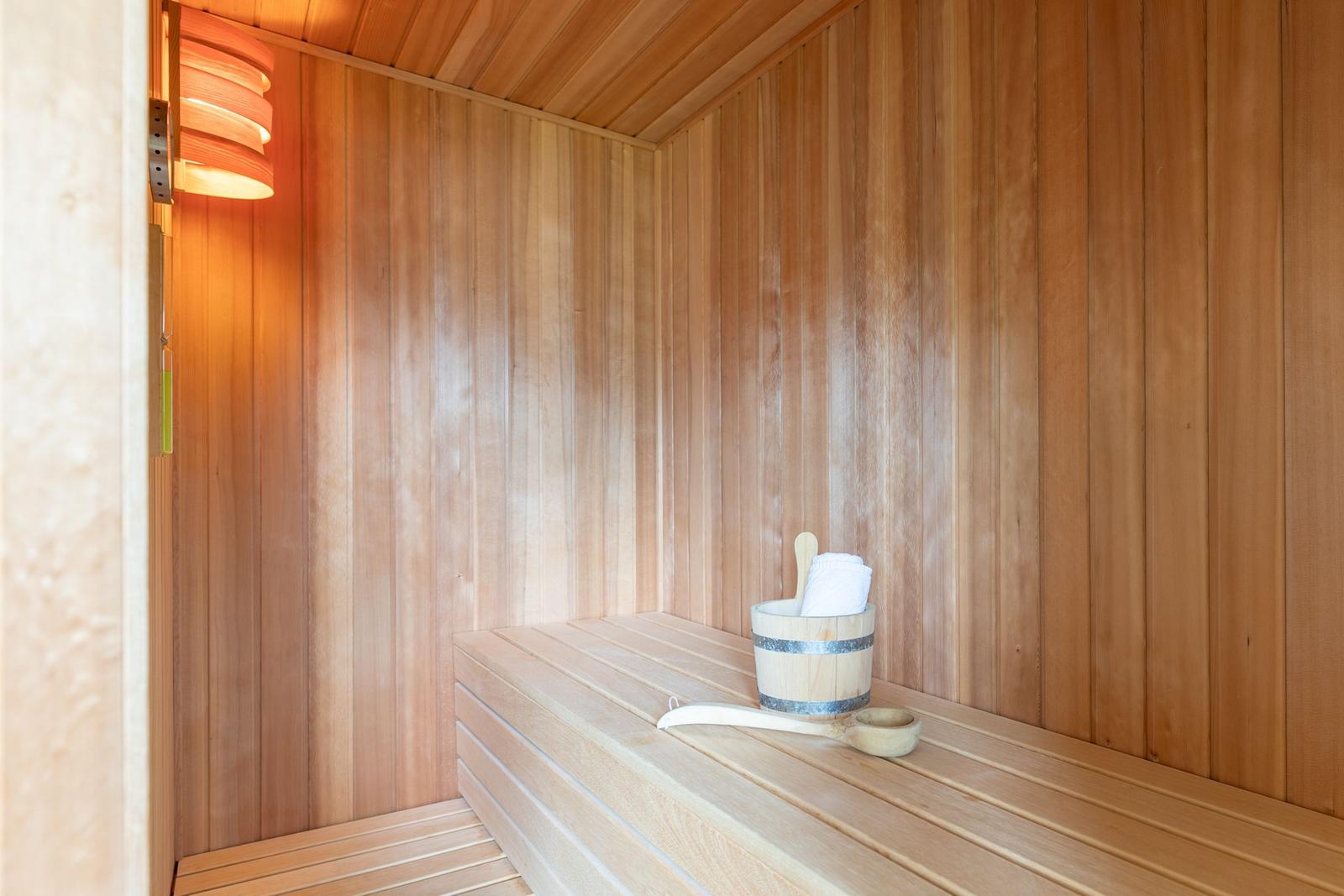 Sauna mit Holzwand, Sitzbank und Eimer mit Handtuch.