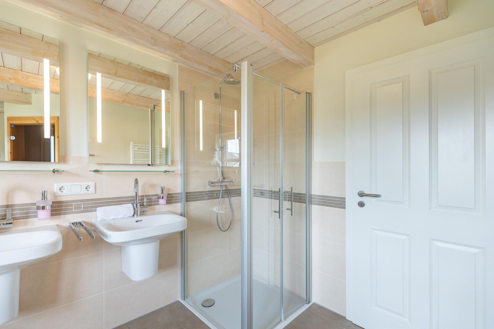 Badezimmer mit Dusche, Waschbecken und Spiegel unter Holzbalkendecke