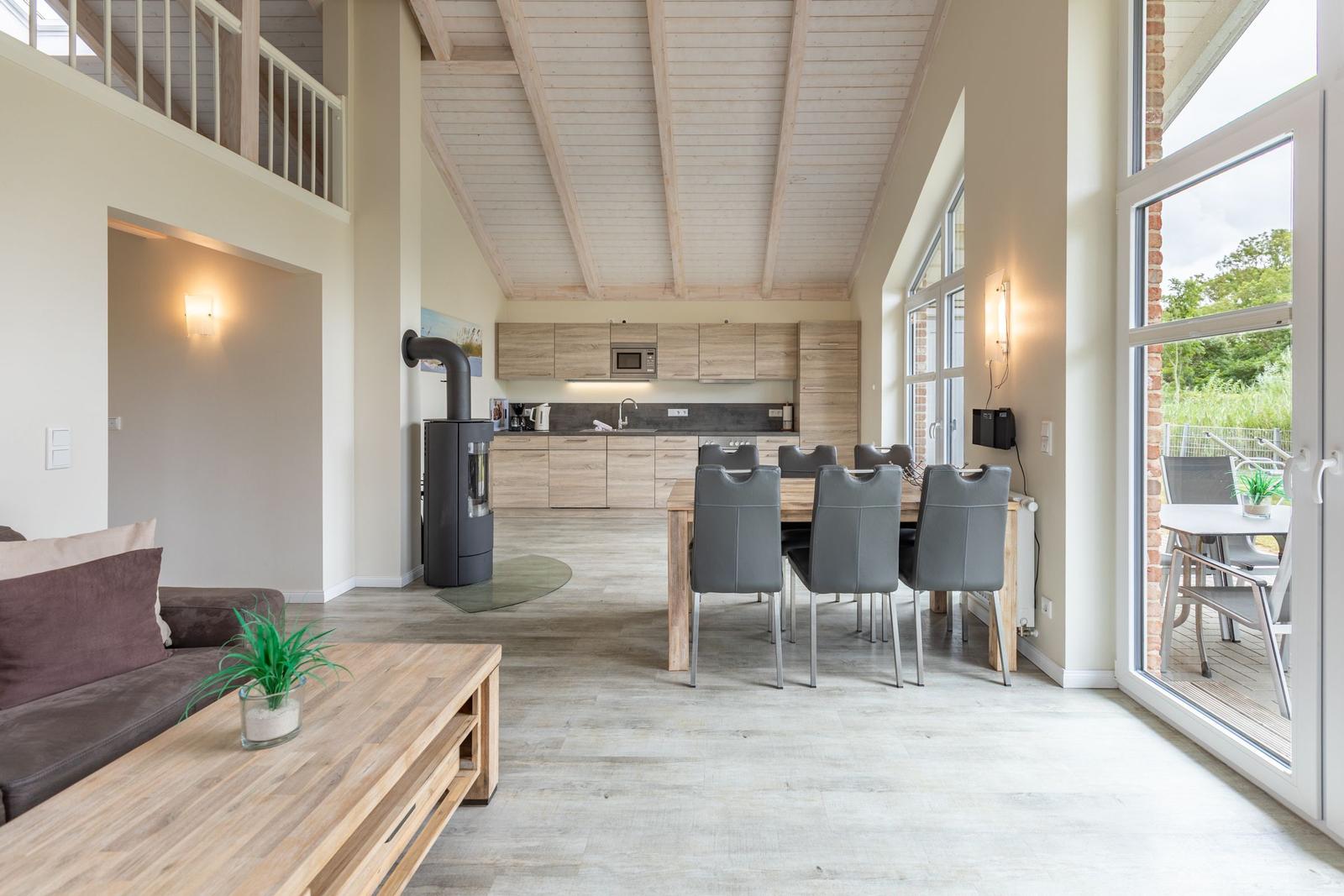 Wohn- und Essbereich mit Küche und Terrasse. Holzdecke und große Fenster.