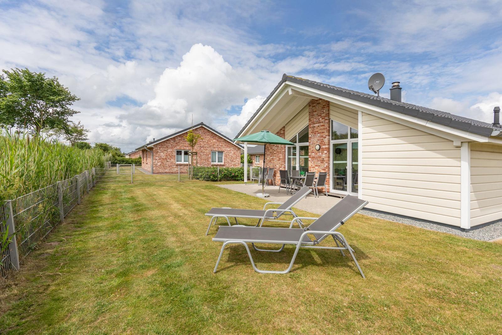 Haus mit Garten, Liegestühlen und Terrasse unter grünem Sonnenschirm.