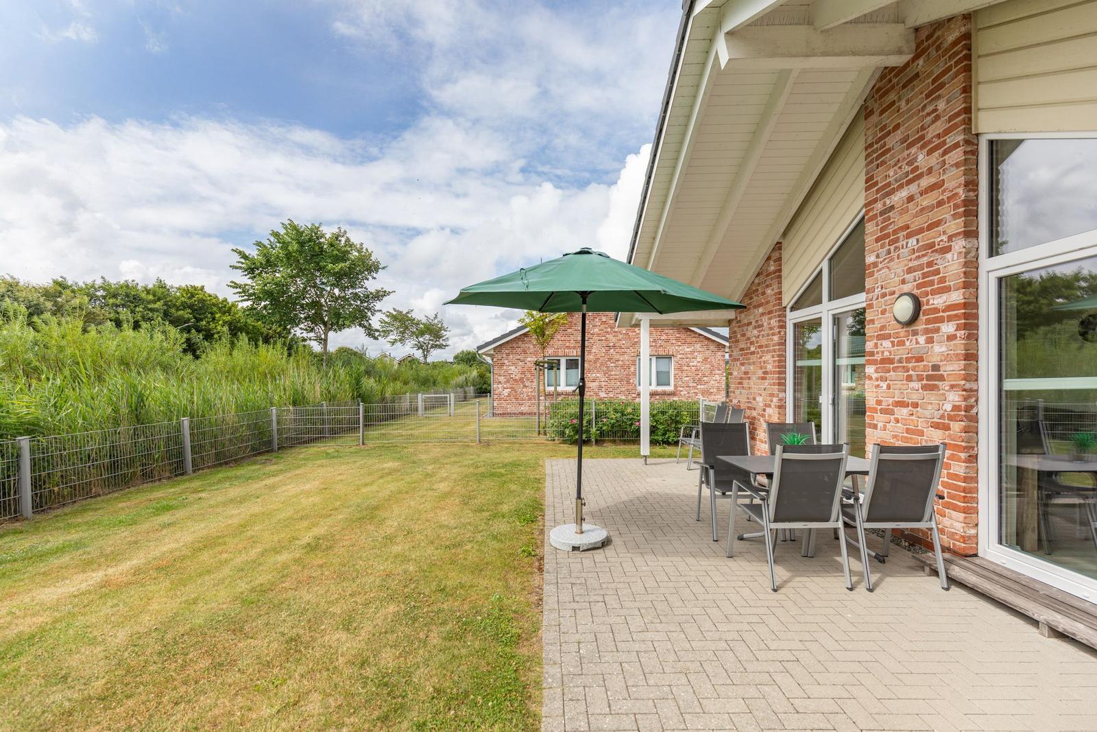 Terrasse mit Tisch, Stühlen und grünem Sonnenschirm neben Haus mit Backsteinmauer.