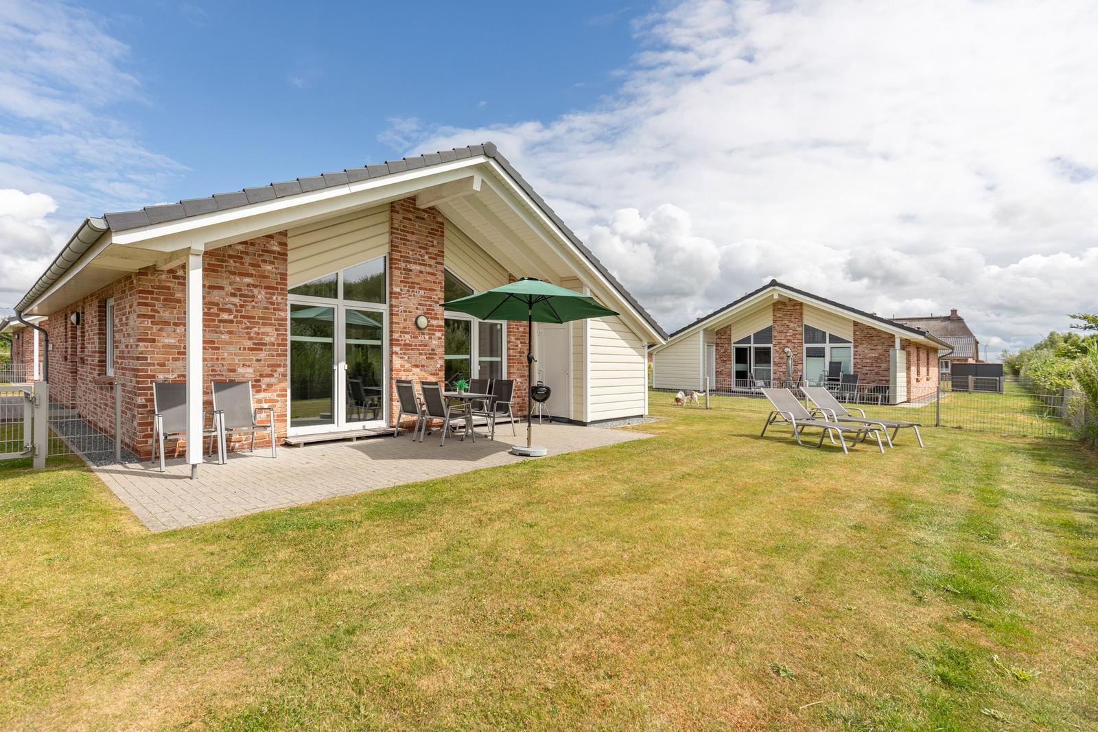 Haus mit Terrasse, Grill und Liegestühlen auf grünem Rasen.