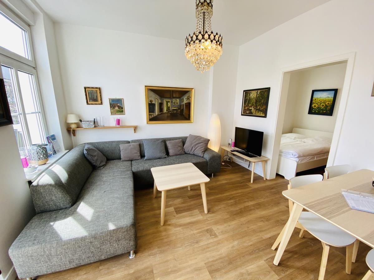 Wohn- und Essbereich mit Sofa, Tisch und TV. Schlafzimmer mit Bett sichtbar.