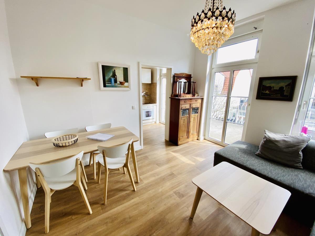 Wohn- und Essbereich mit Tisch, Stühlen, Sofa und Kronleuchter. Durchgang zur Küche.