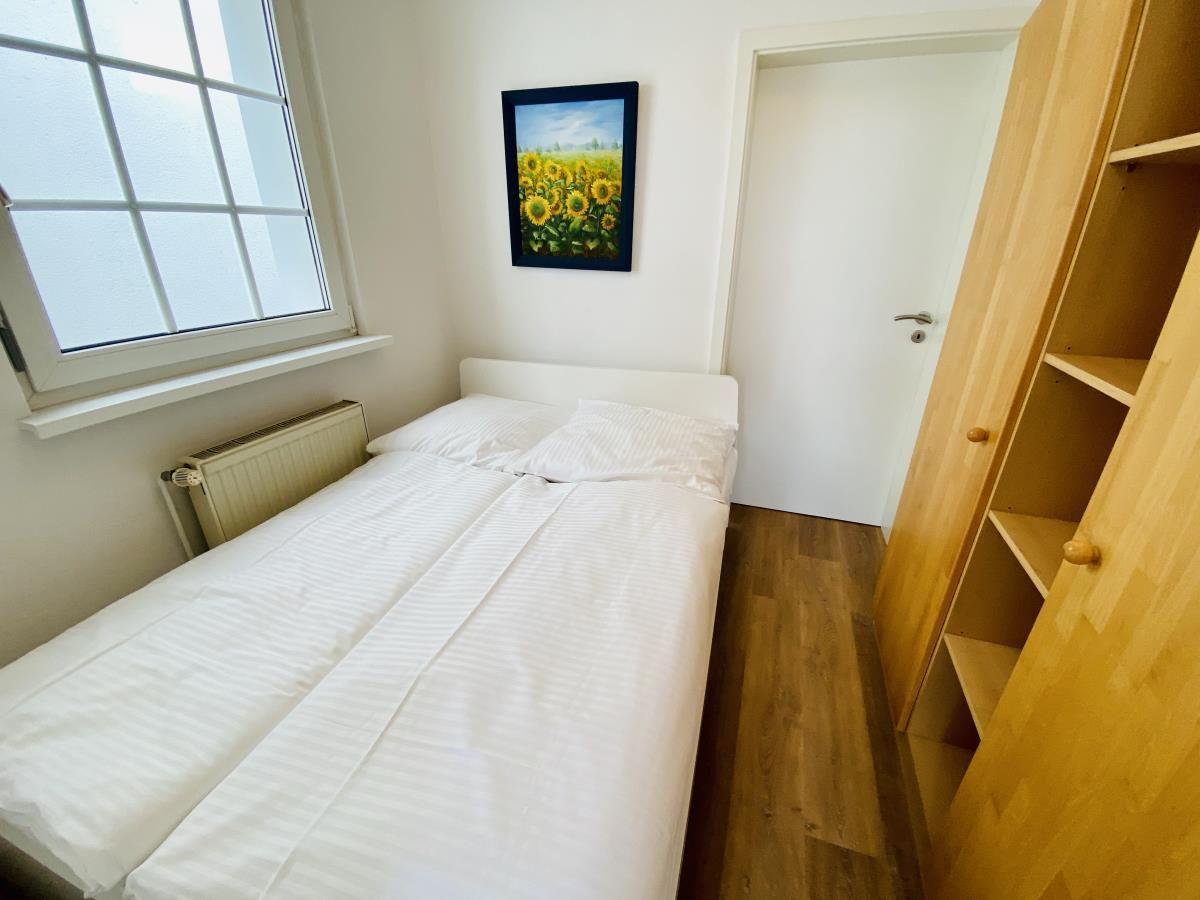 Schlafzimmer mit Bett, Holzregal und Fenster. Wandbild zeigt Sonnenblumen.