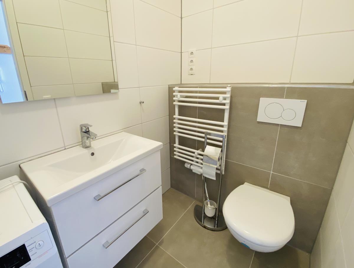 Badezimmer mit Waschbecken, Spiegel, Toilette und Heizkörper