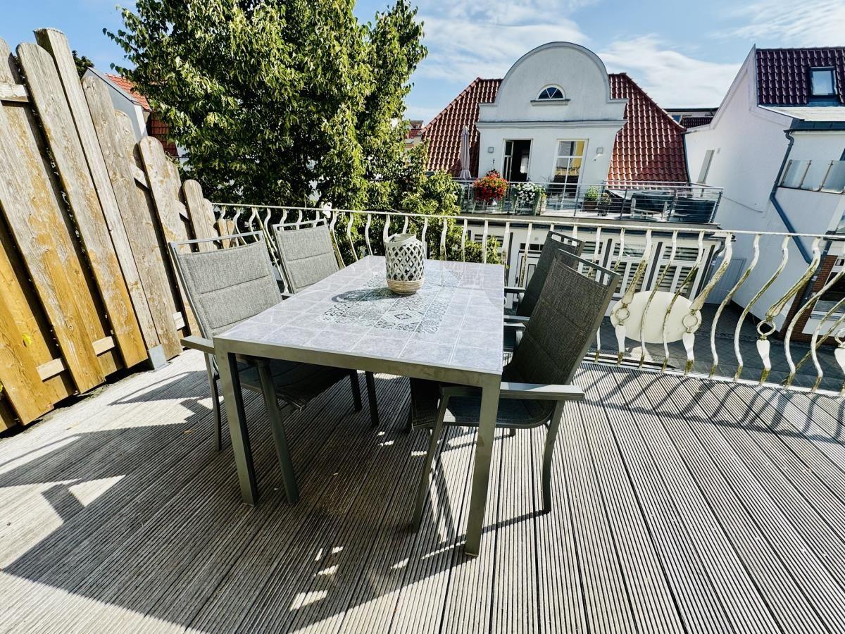 Terrasse mit Tisch und Stühlen, Holzboden und Geländer, Blick auf Wohnhäuser.