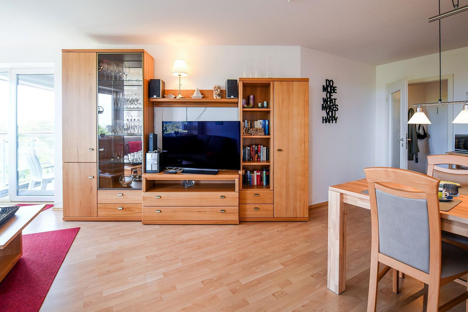 Wohn- und Essbereich mit Holzmöbeln, TV und Balkonzugang.