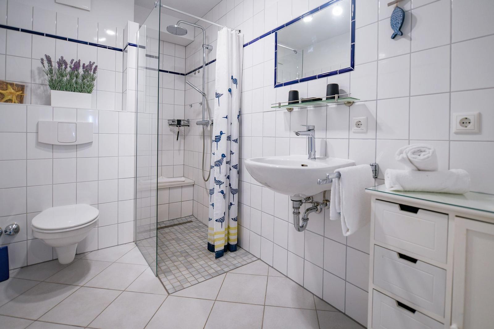 Badezimmer mit Dusche, Waschbecken und Toilette. Weiße Fliesen und blauer Akzent.