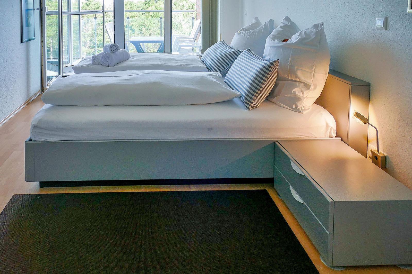 Schlafzimmer mit Doppelbett, Nachttisch und Balkonansicht.