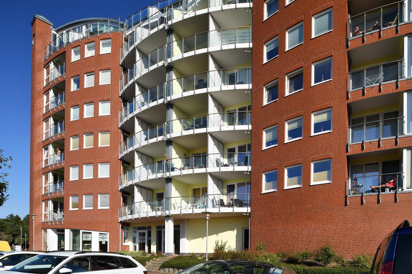 Mehrfamilienhaus mit Balkonen und Fenstern. Einige Bewohner sitzen auf den Balkonen.