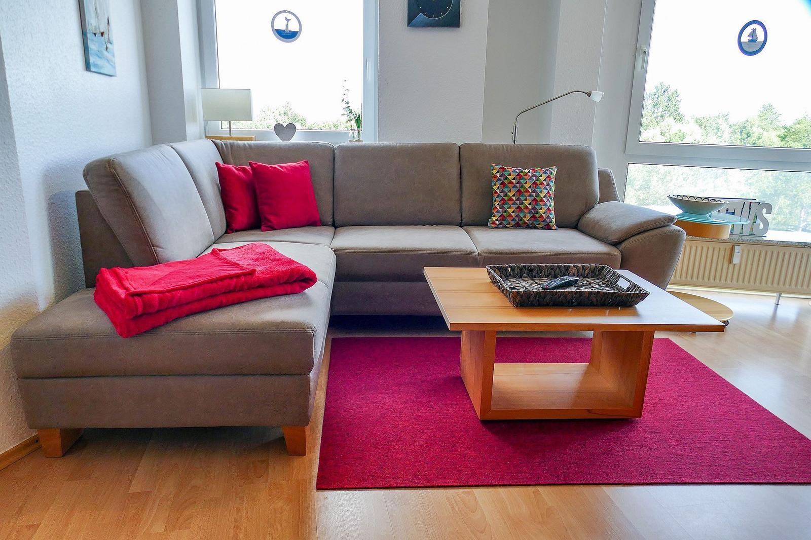 Ein Wohnzimmer mit grauem Sofa, rotem Teppich und Holztisch.