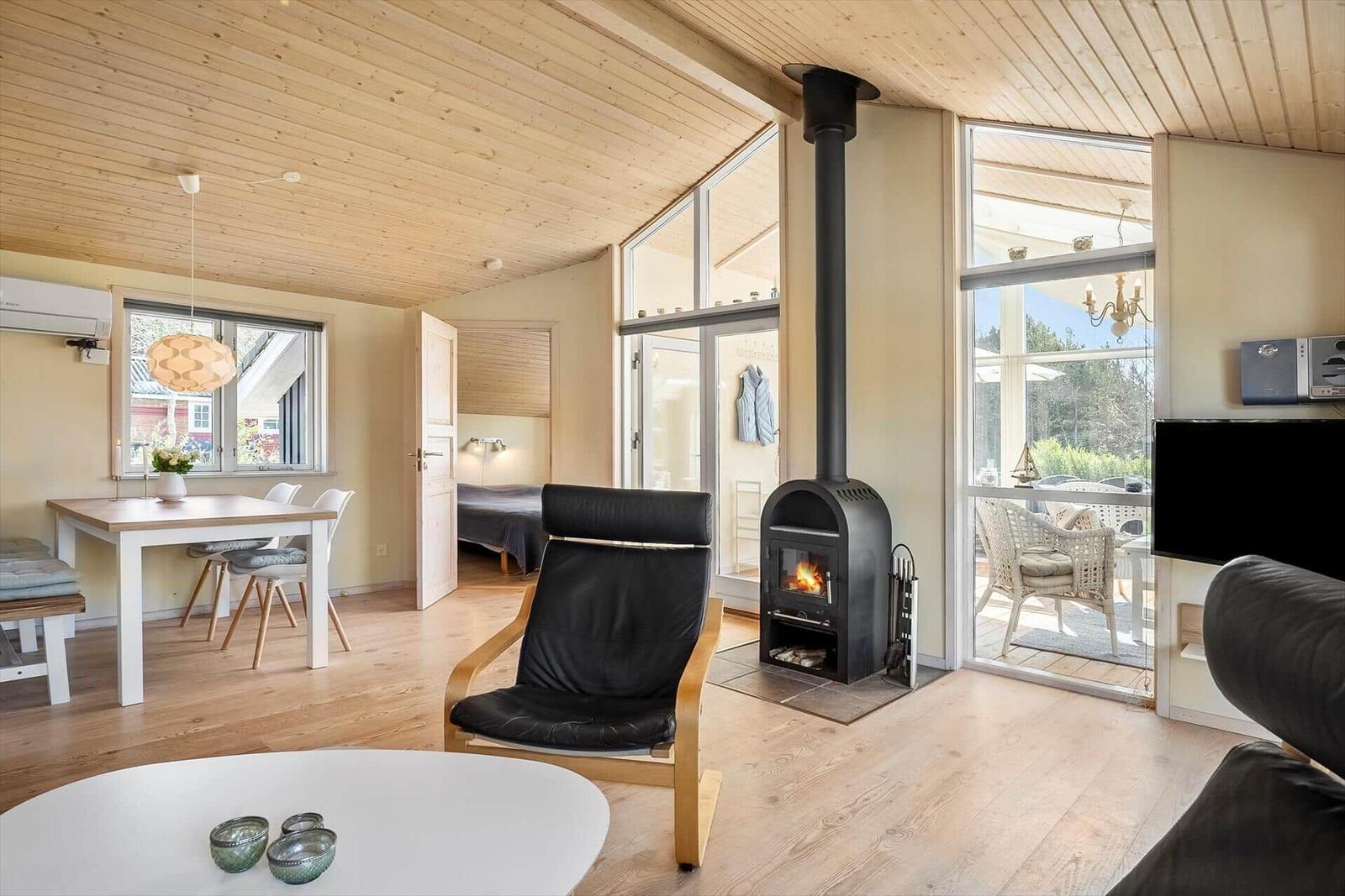 Wohnraum mit Kamin, Essbereich und Terrasse. Holzdecke und -boden.