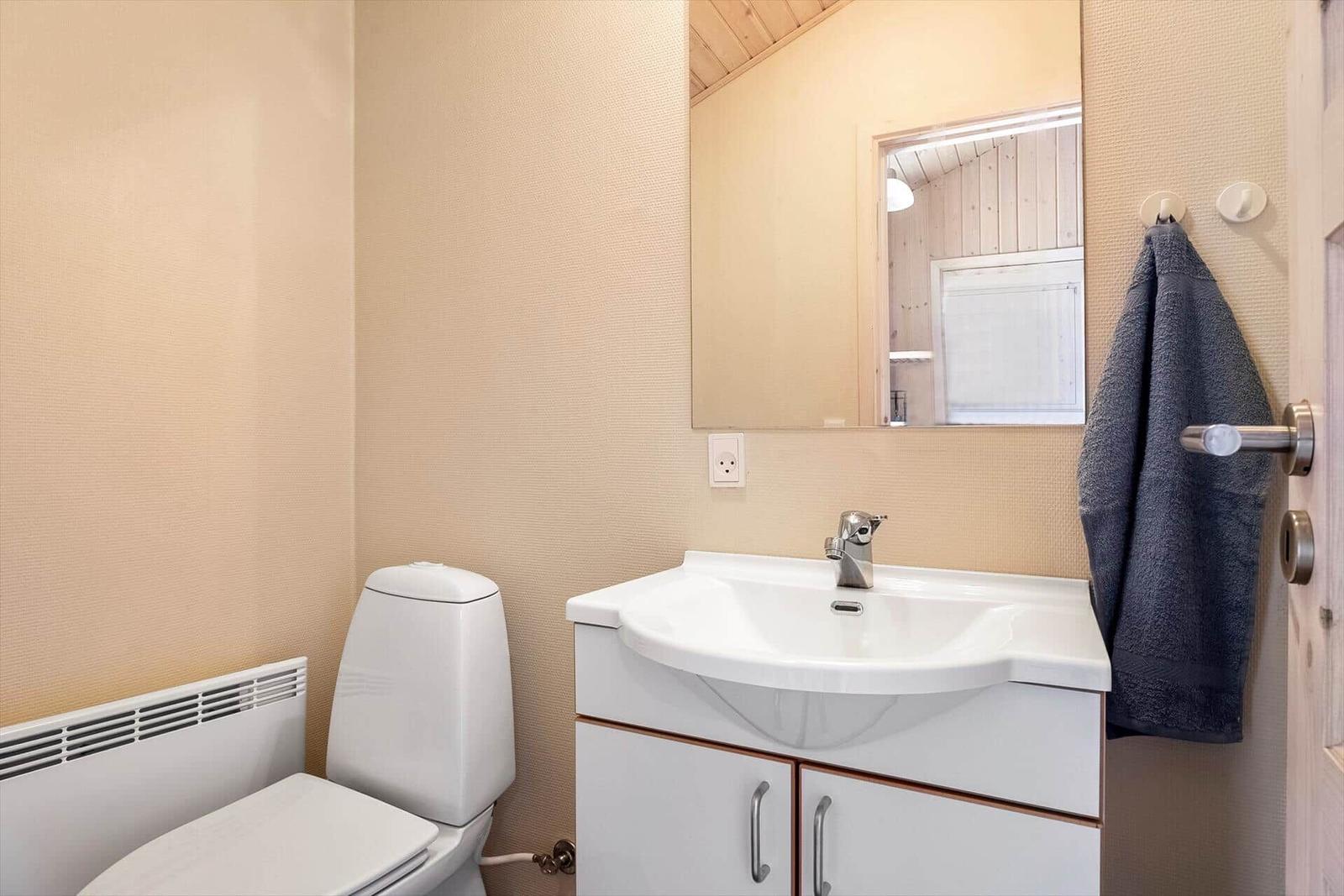 Badezimmer mit Waschbecken, Spiegel und Toilette. Handtuch hängt an der Tür.