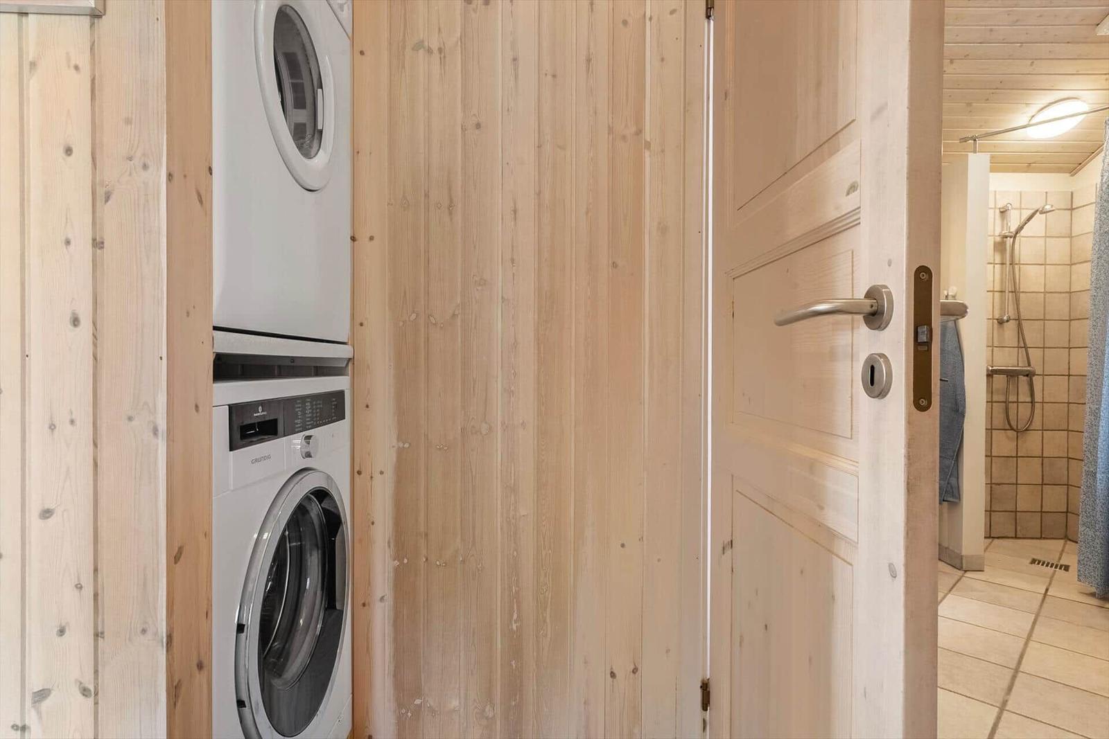 Wäscherei mit Waschmaschine und Trockner. Tür führt in Bad mit Dusche.