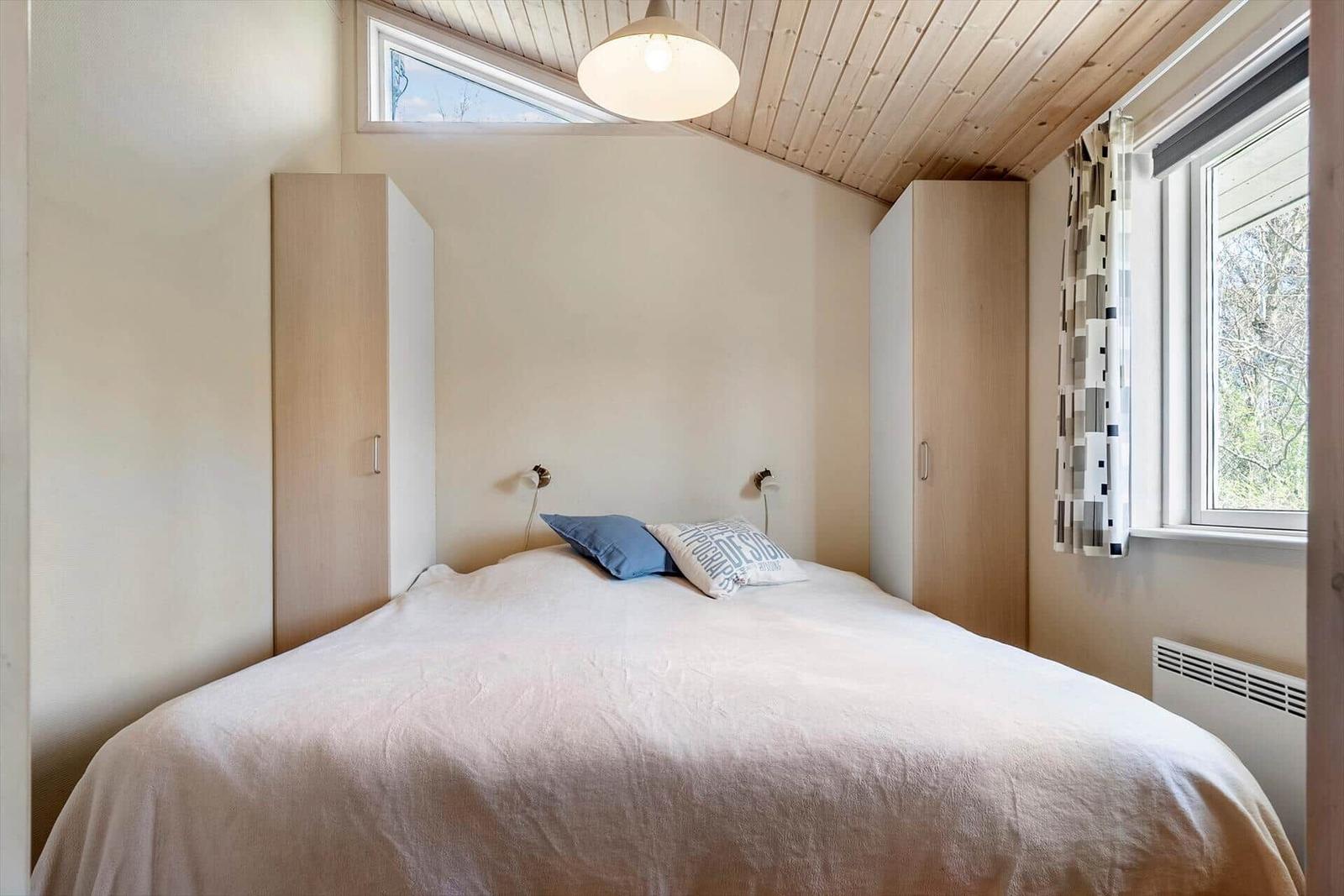 Schlafzimmer mit Bett, Kleiderschränken und Fenstern.