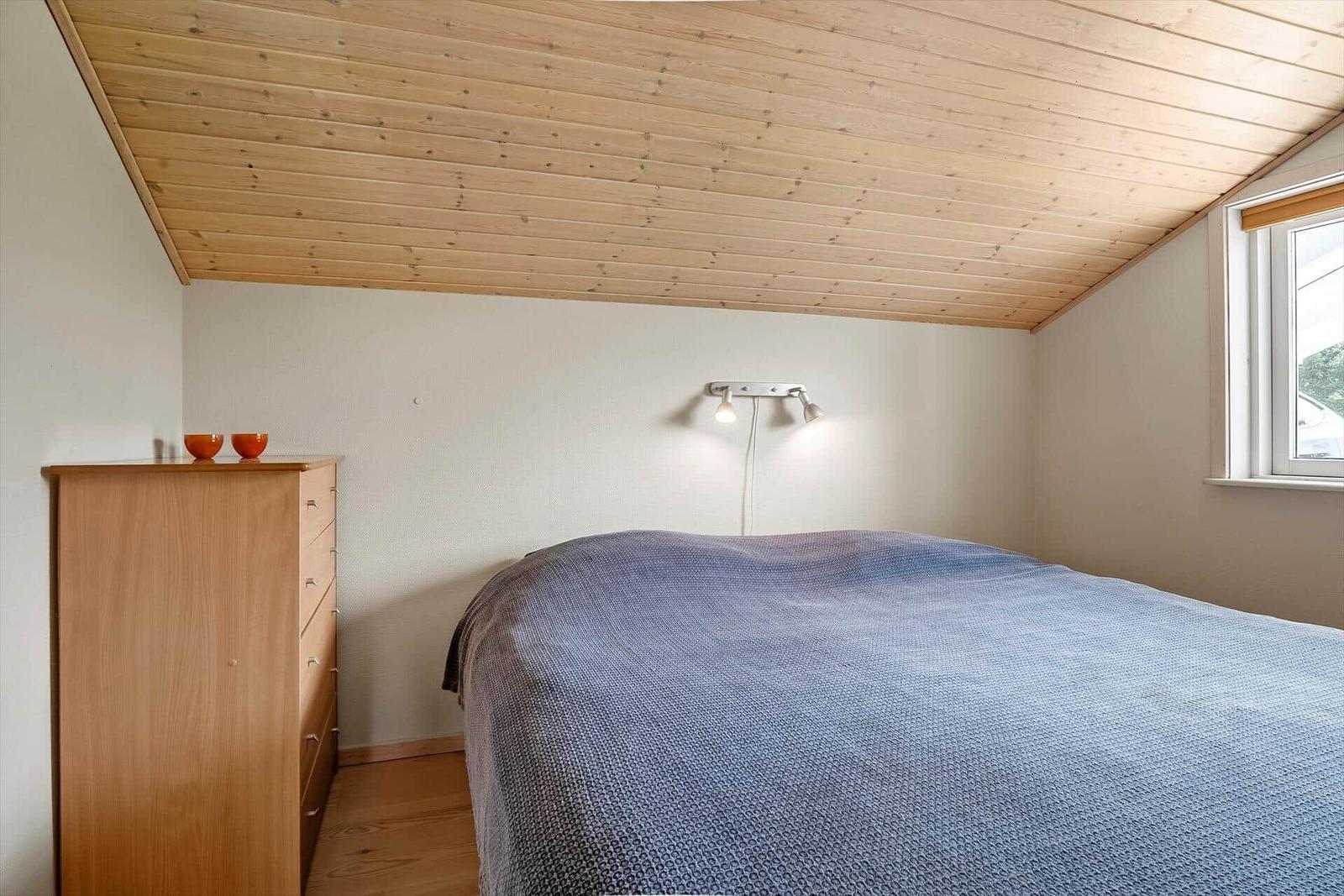 Schlafzimmer mit Holzdecke, Bett und Kleiderschrank. Fenster mit Blick nach draußen.
