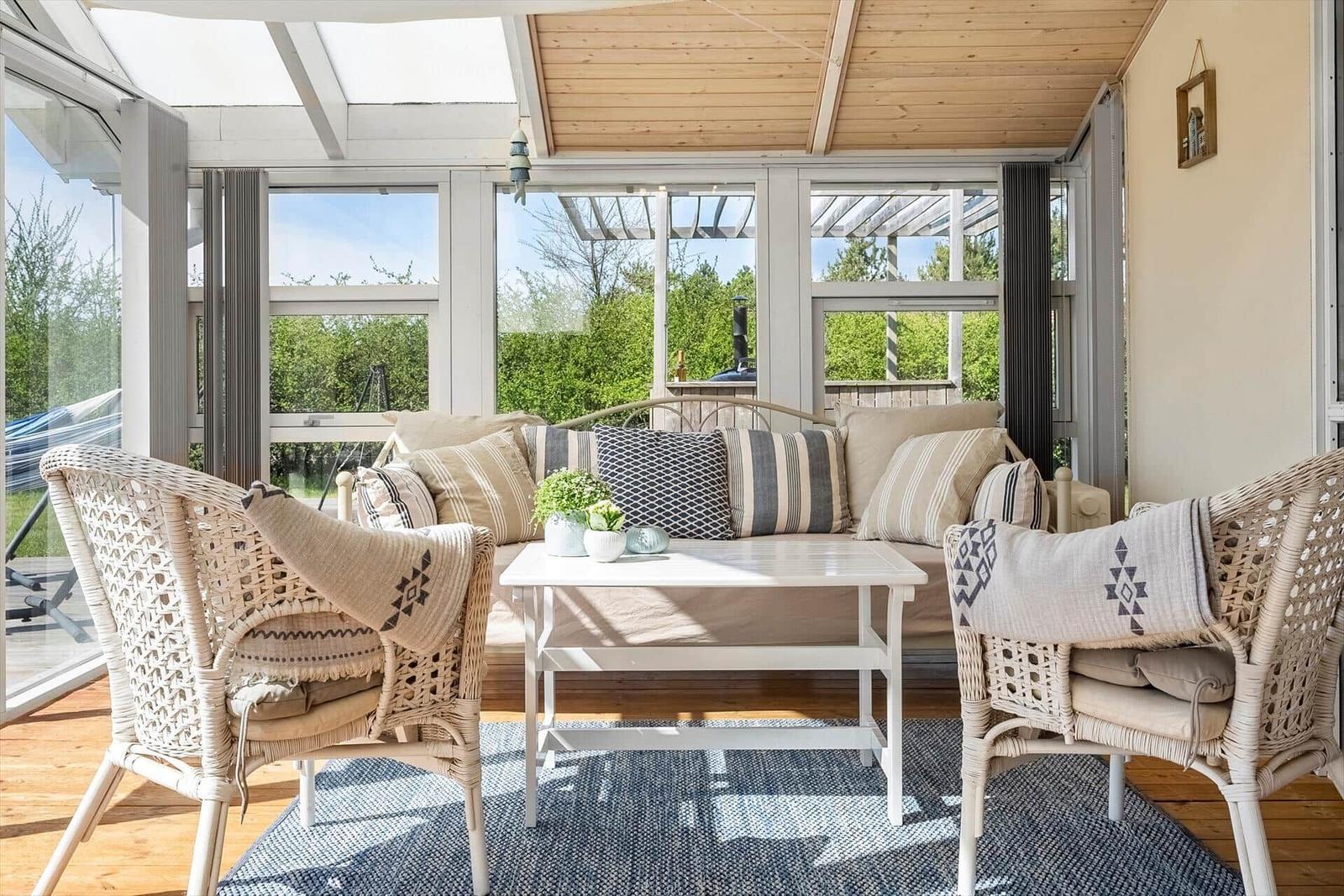 Sitzbereich mit Wickerstühlen und Sofa unter Glasdach mit Blick auf Garten.