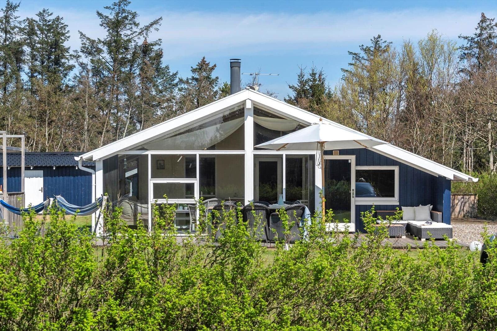 Ein Haus mit blauer Fassade und großem Glasbereich. Außenbereich mit Tisch, Stühlen und Sonnenschirm.