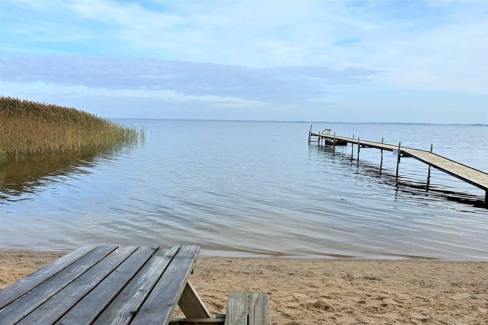 Holztisch am Strand mit Blick auf einen Steg ins Wasser.
