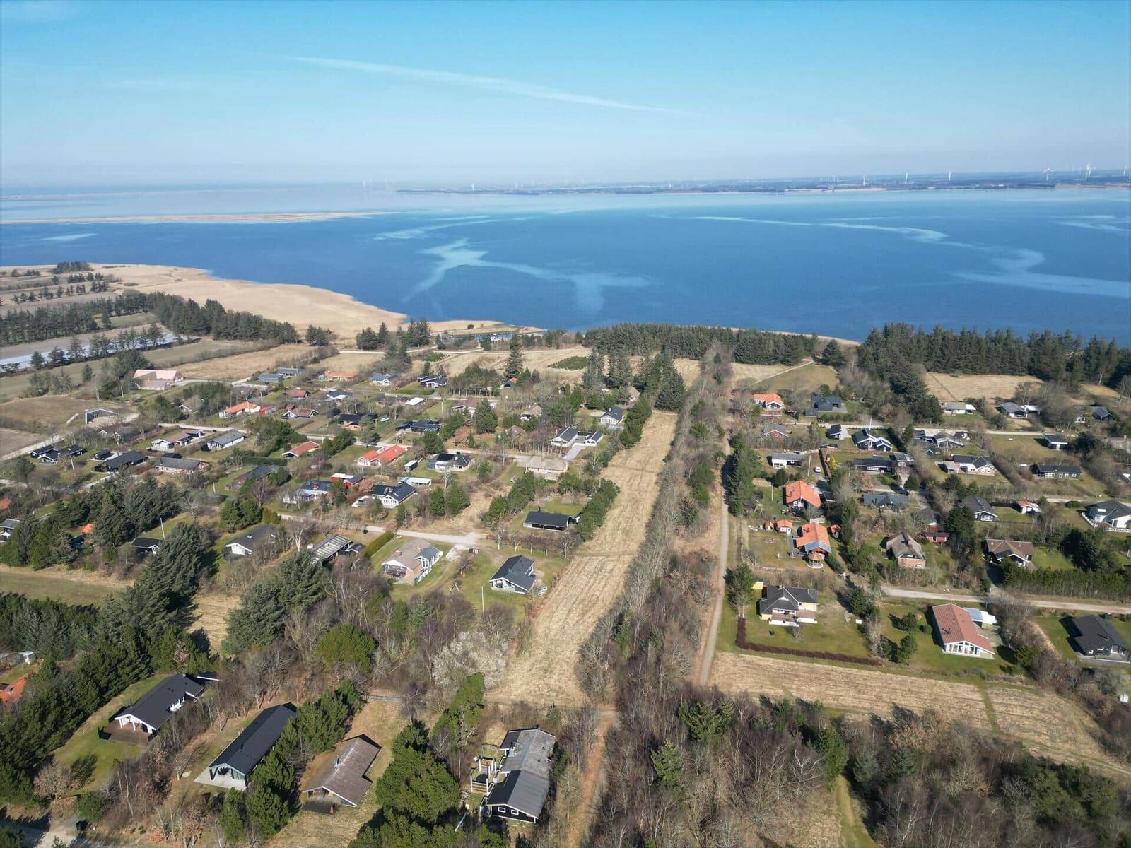 Luftbild einer Küstenlandschaft mit Häusern und einem großen Gewässer im Hintergrund.
