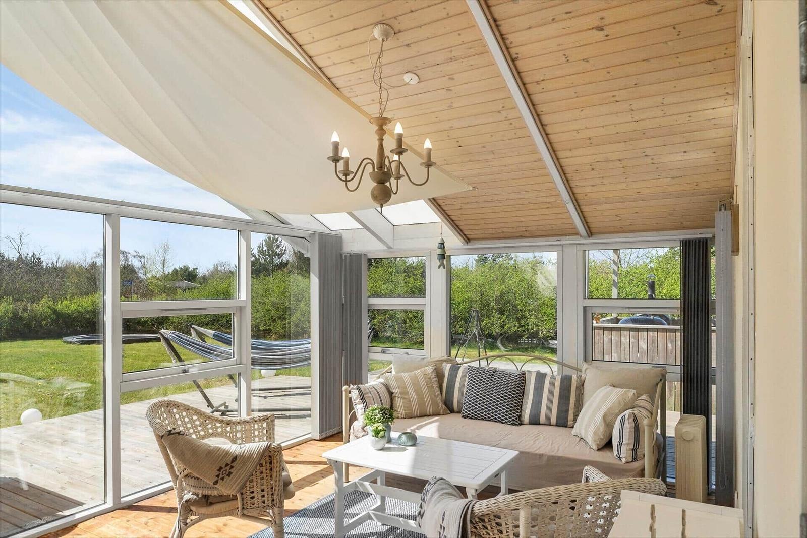 Terrassenbereich mit Sofa, Stühlen und Tisch unter Holzdecke mit Blick auf Garten.