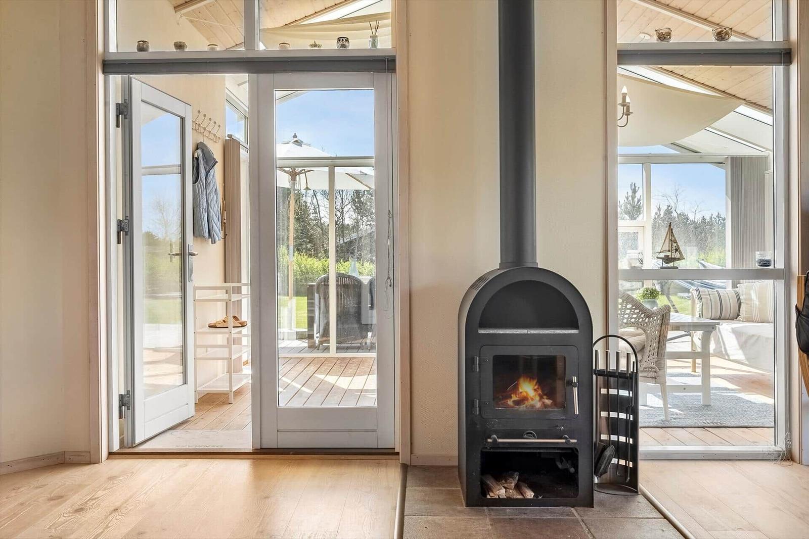 Innenraum mit Kaminofen, Terrasse und Sitzbereich. Durchgänge zu Außenbereich.